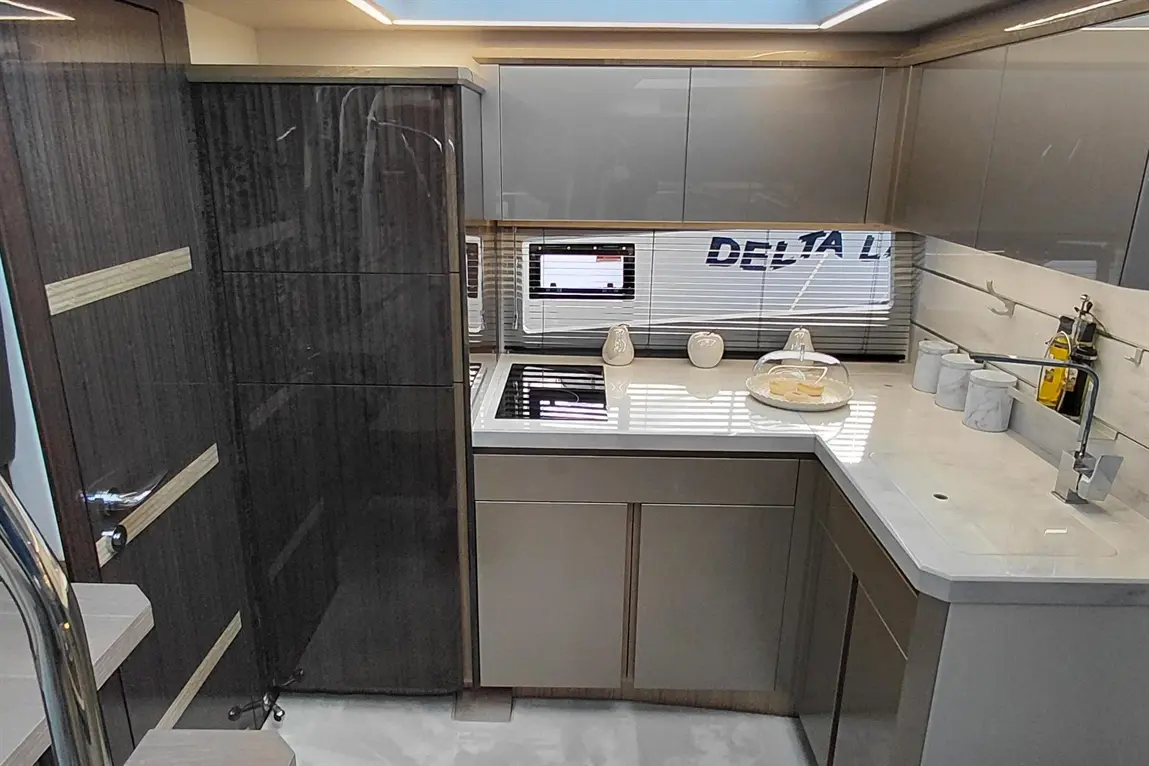Modern kitchen with sleek grey cabinets, stovetop, and marble countertop, featuring a plate of pastries and a wall-mounted screen.
